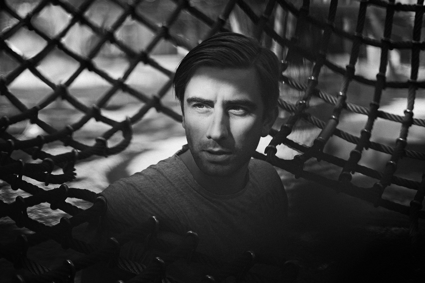 Portrait eines Mannes in Schwarz-Weiß vor einem Netz, kreative People-Fotografie.