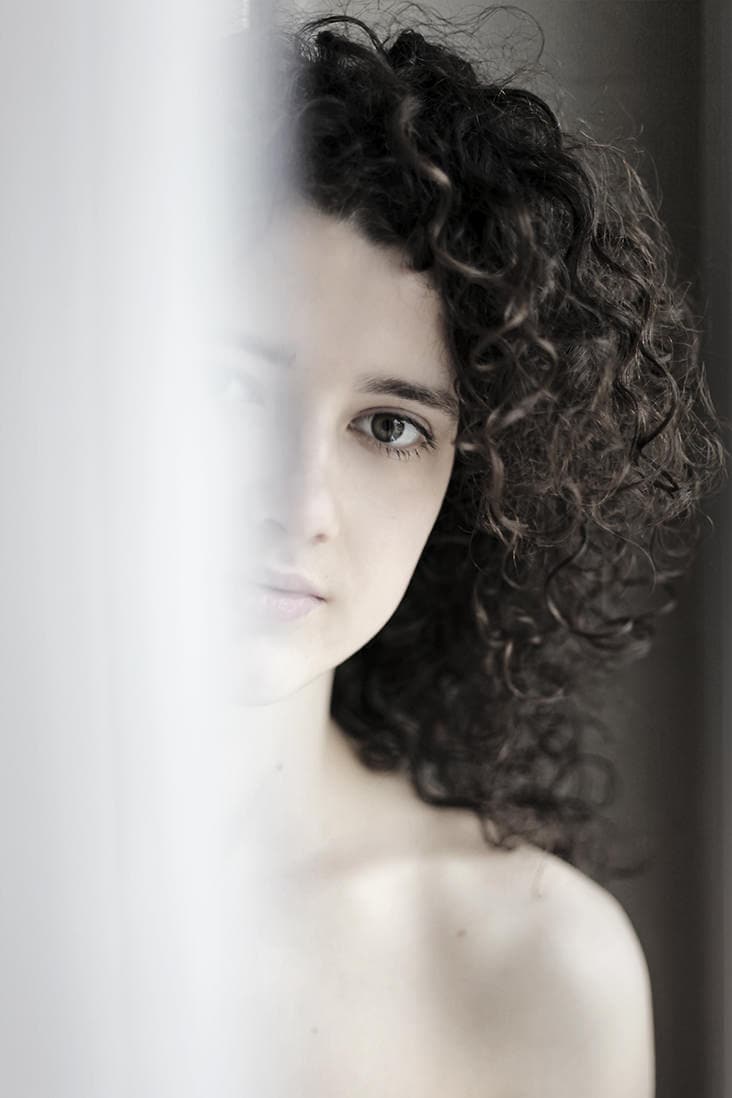 Porträt einer jungen Frau mit lockigem Haar, Blick seitlich, künstlerische Schwarz-Weiß-Fotografie.