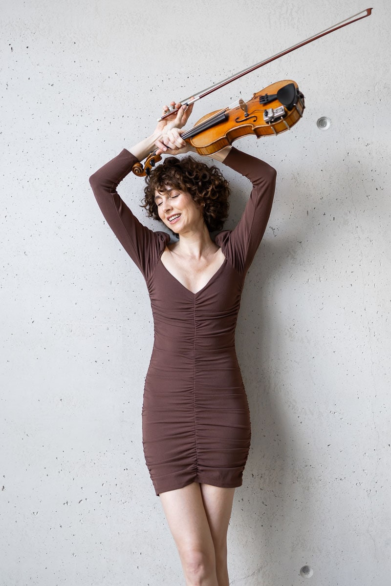 Frau spielt Geige gegen grauen Betonwand, elegante Kleidung, kreative Fotografie.