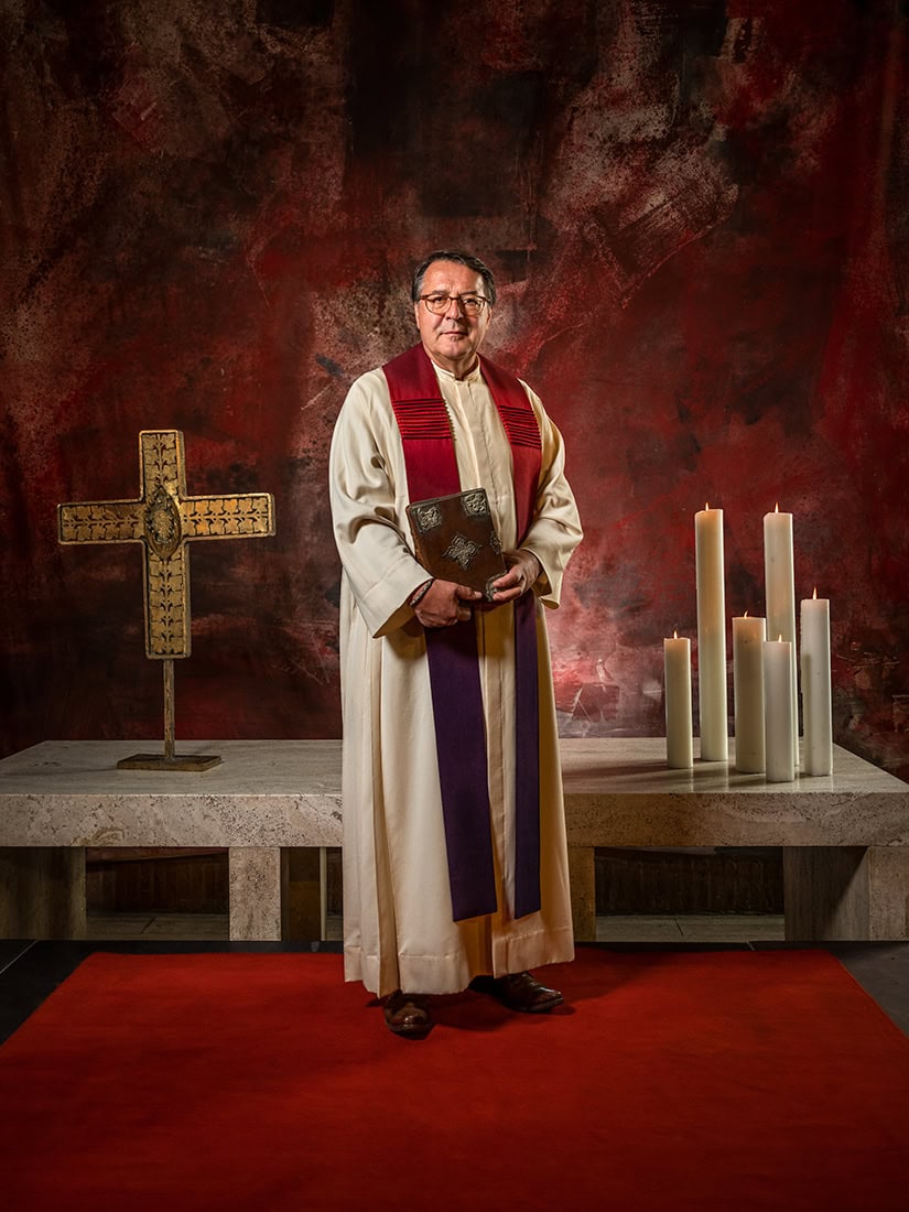 Pfarrer in Kirche mit Bibel, Kerzen und Kreuz, professionelle Fotografie, Köln.
