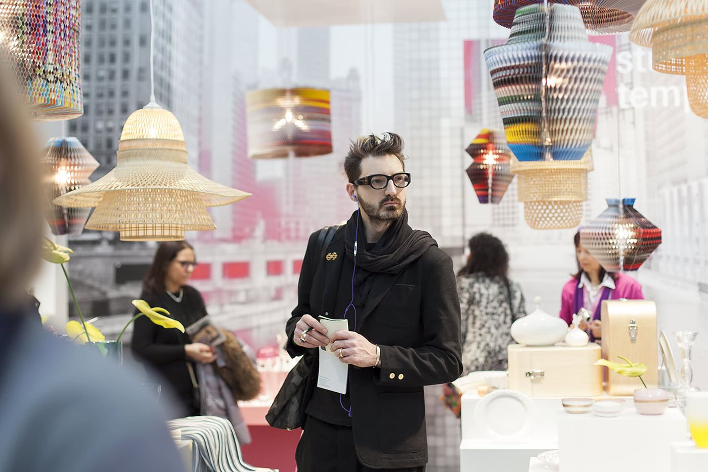 Mann mit Brille und dunklem Mantel bei Lampen- und Lichtketten-Ausstellung.
