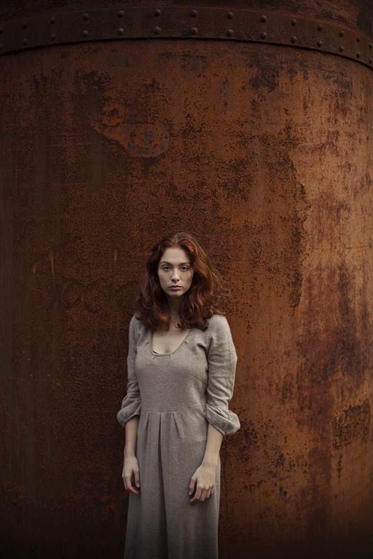 Frau in grauem Kleid vor rostiger Metallwand in Köln, urbanes Fotografie-Setting.