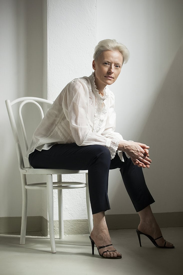 Elegante Porträtaufnahme einer älteren Frau in modernem Studio, sitzend auf weißem Stuhl.