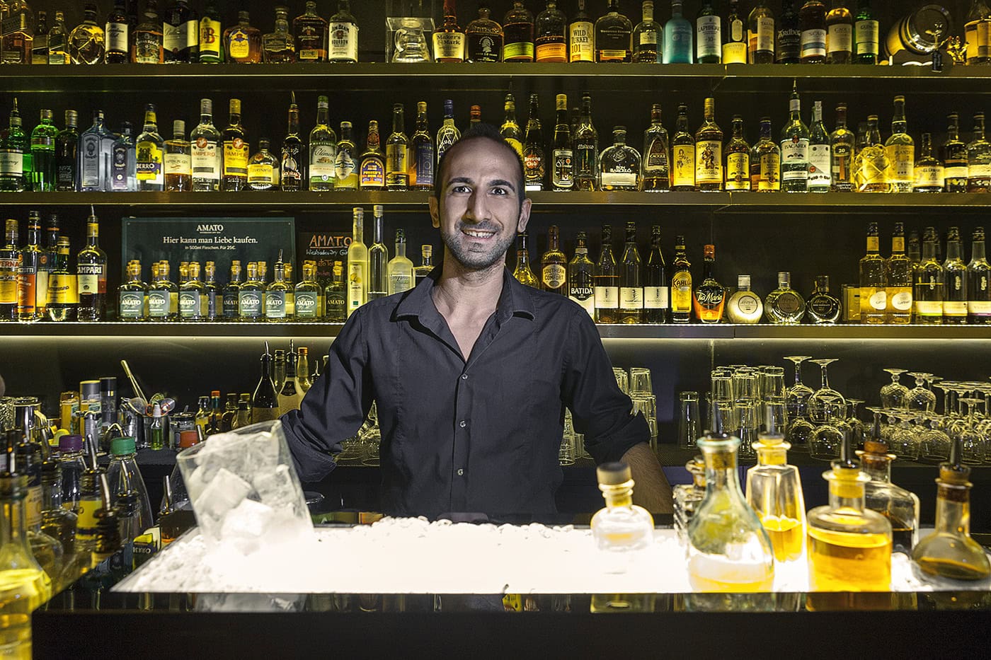 Barkeeper hinter der Bar mit Spirituosen und Gläsern, professionell fotografiert.