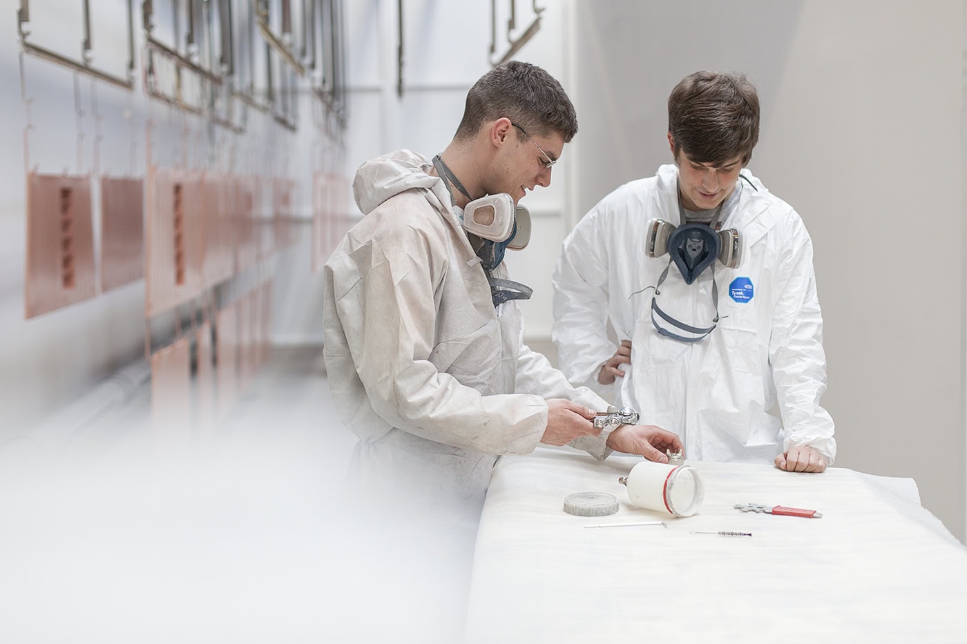 Zwei junge Männer in Schutzkleidung bei technischer Arbeit in einem Labor.