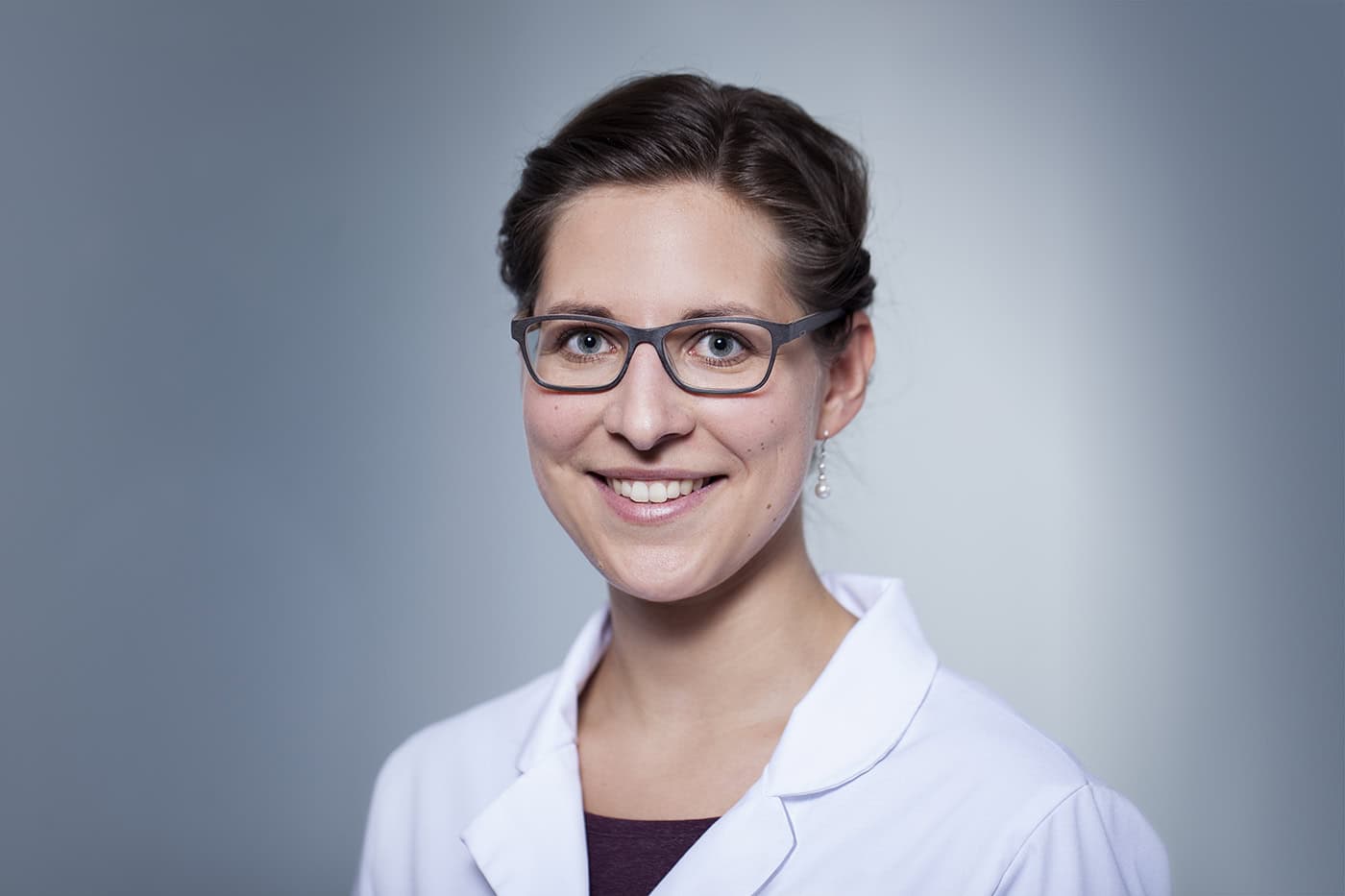 Freundliche Ärztin in Weiß mit Brille, professionell und vertrauenswürdig.