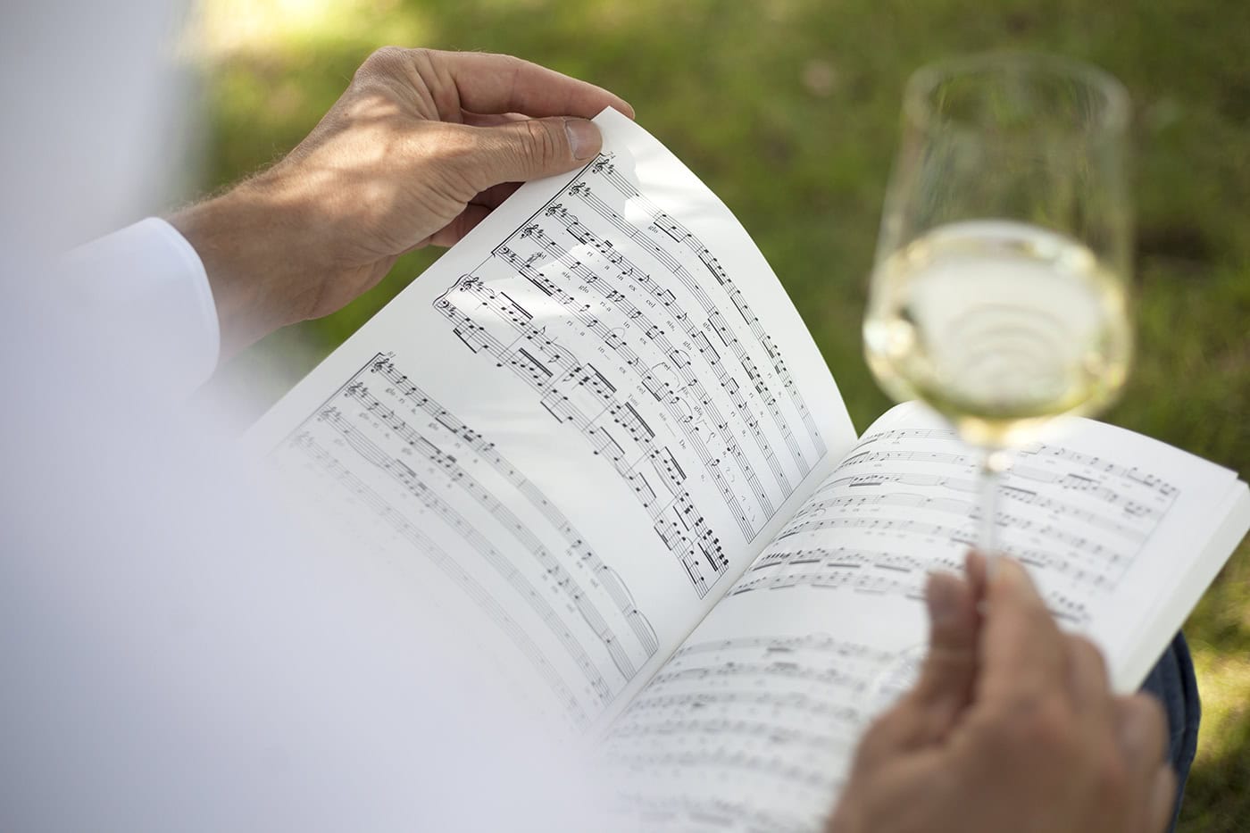 Musiker liest Notenblatt im Freien mit einem Glas Weißwein in der Hand.