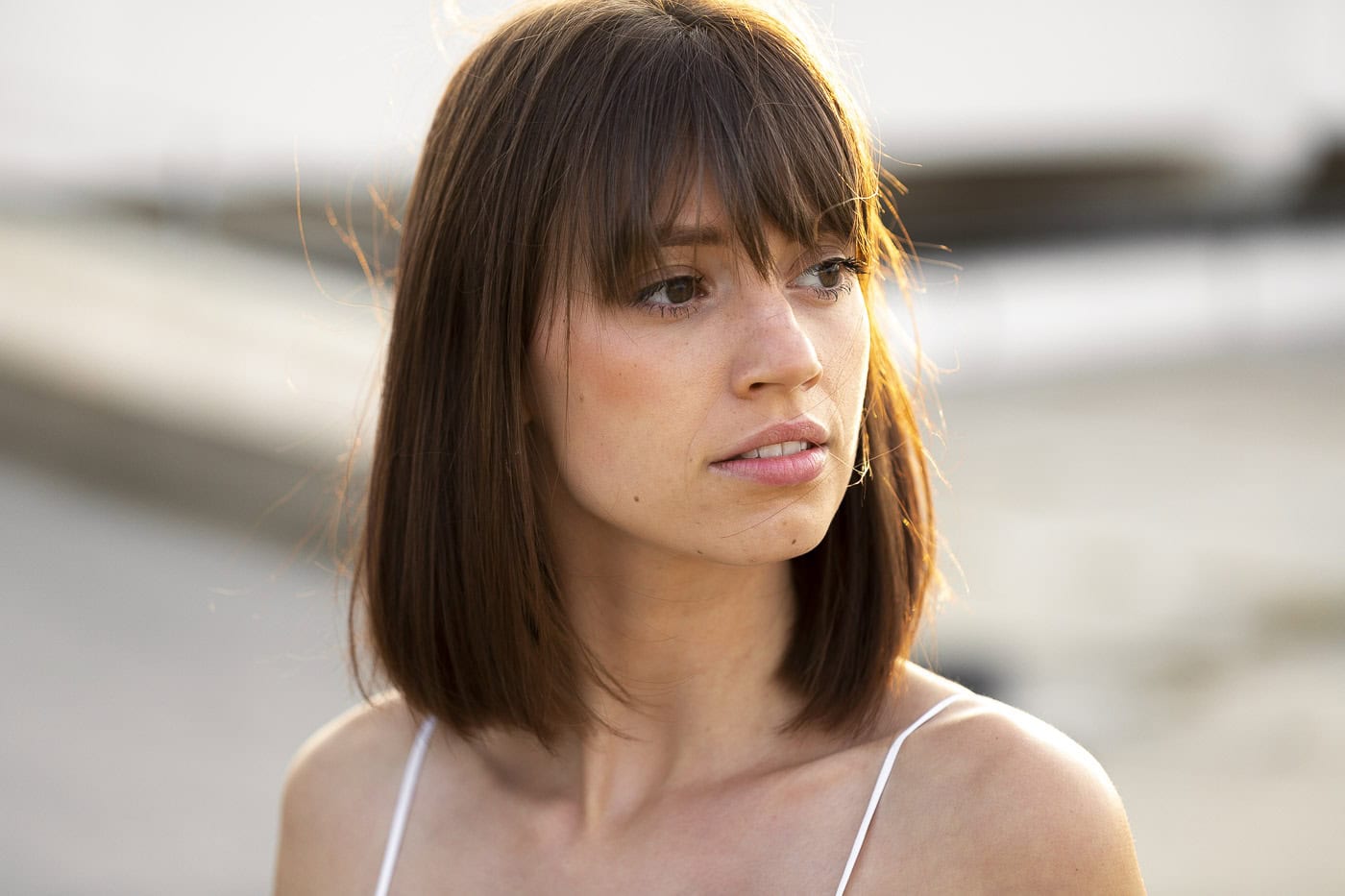Junge Frau mit braunen Haaren und weißen Top am Strand bei Sonnenuntergang.