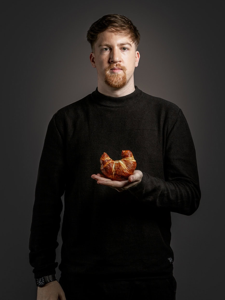 Mann hält Croissant vor dunklem Hintergrund.