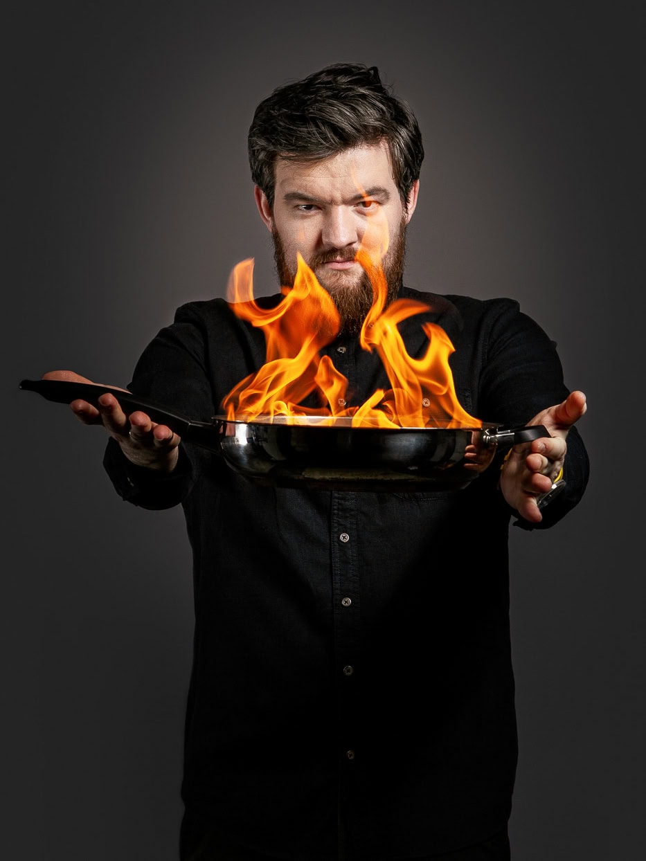 Mann hält eine Pfanne mit brennendem Feuer, kreative Food-Fotografie in Köln.
