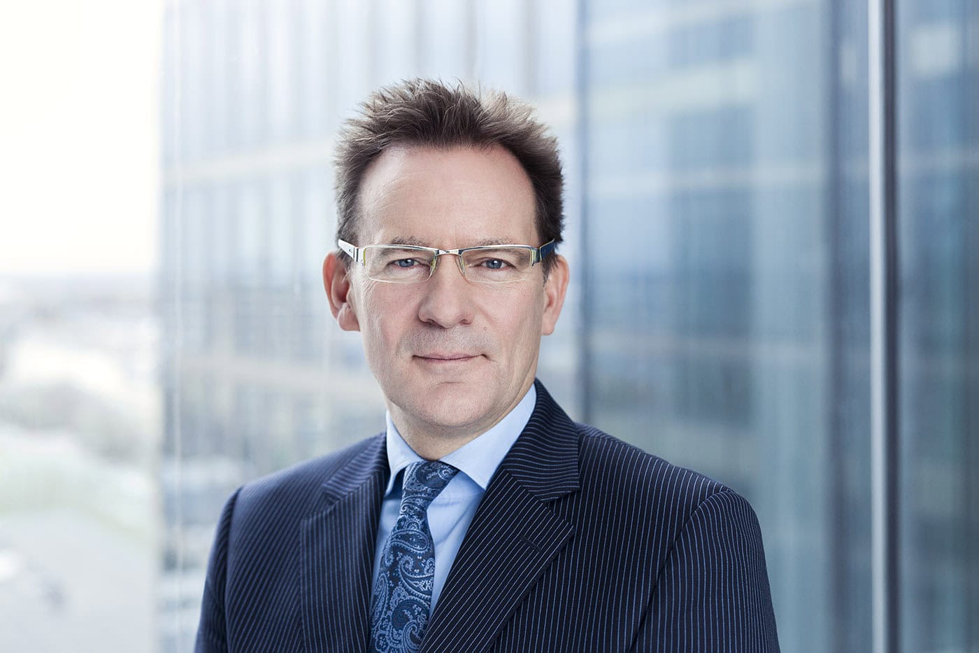 Porträtfotografie eines Mannes in Business-Kleidung vor Glasfassade.