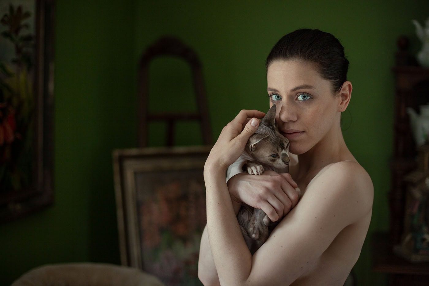 Frau hält Katze vor grünem Hintergrund, kreative Portraitaufnahme.