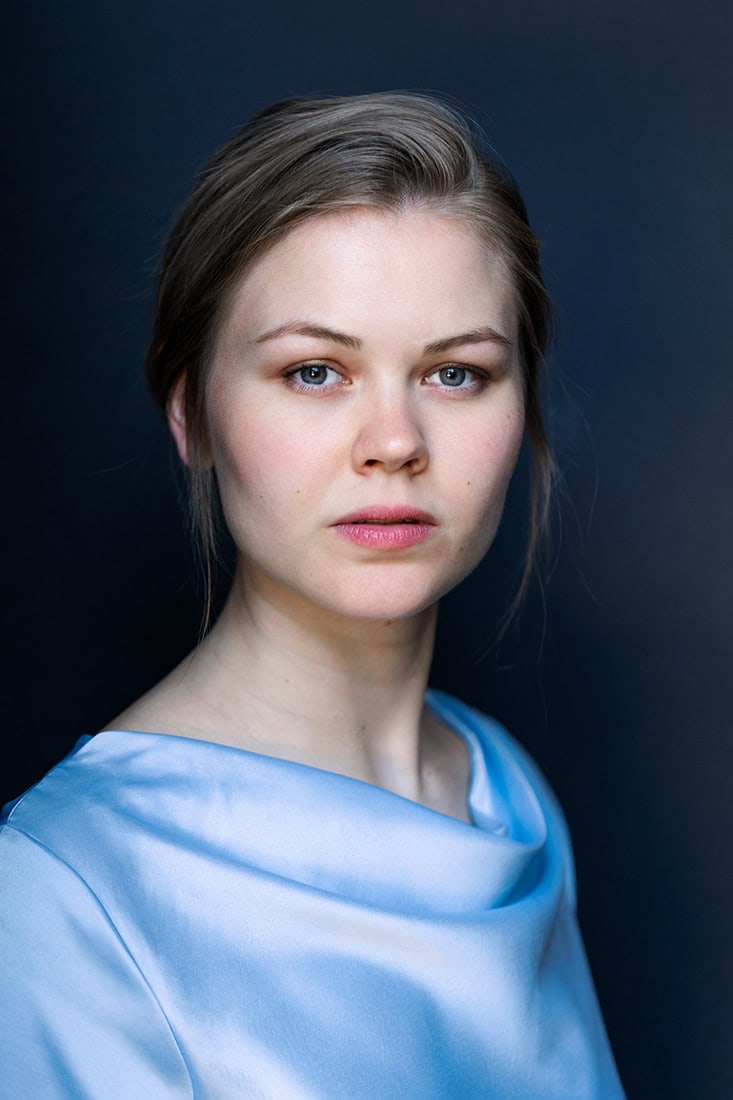 Hochwertiges Portrait einer jungen Frau mit blauer Bluse vor dunklem Hintergrund.