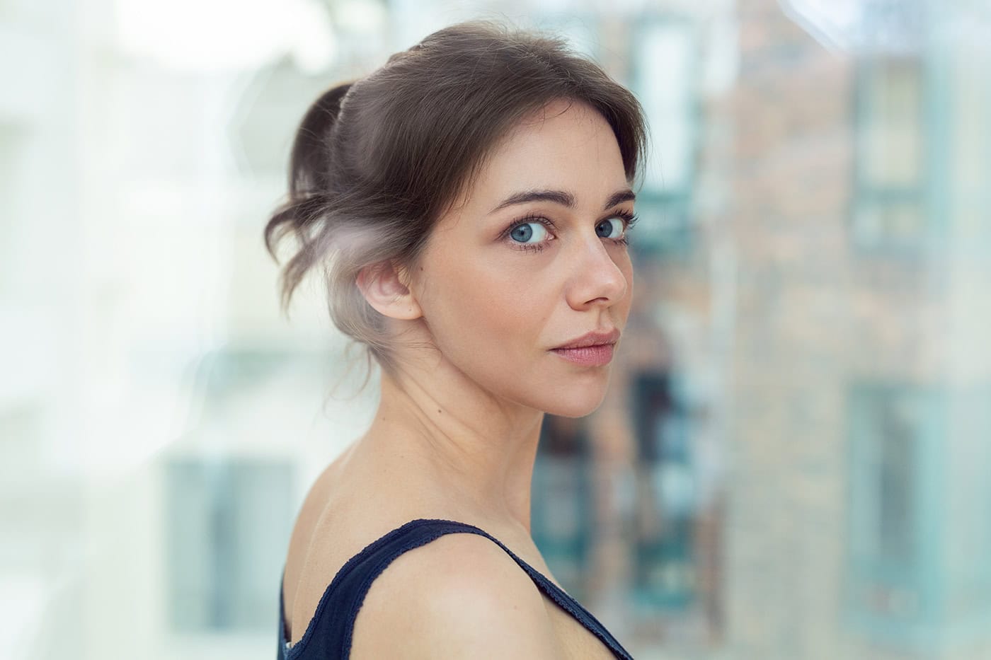Porträt einer jungen Frau mit blauen Augen vor moderner Glasfassade.
