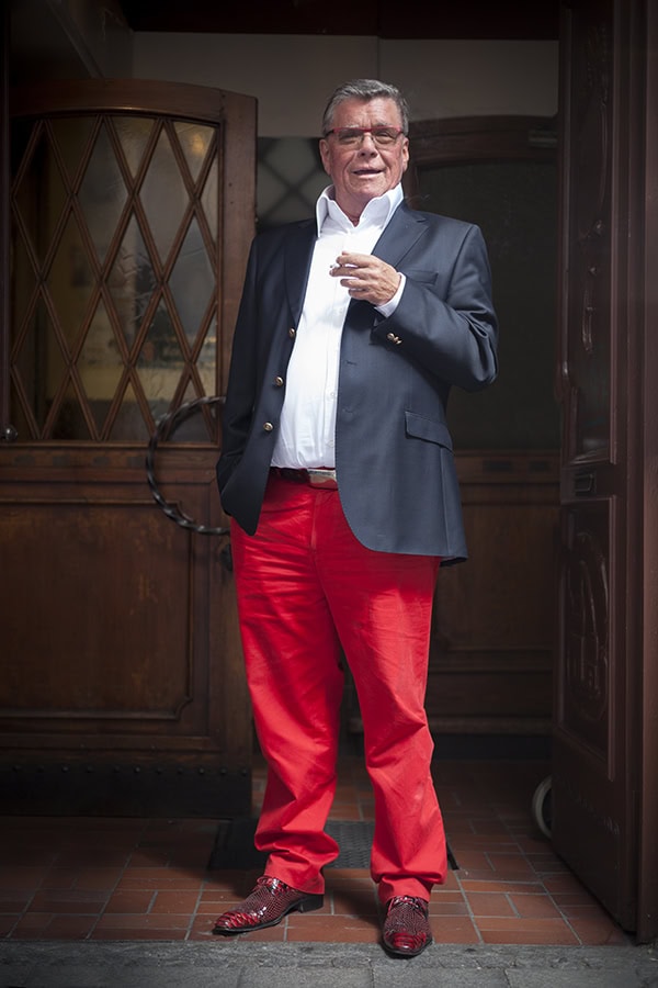 Mann in Anzug und roten Hosen vor historischem Gebäude in Köln.