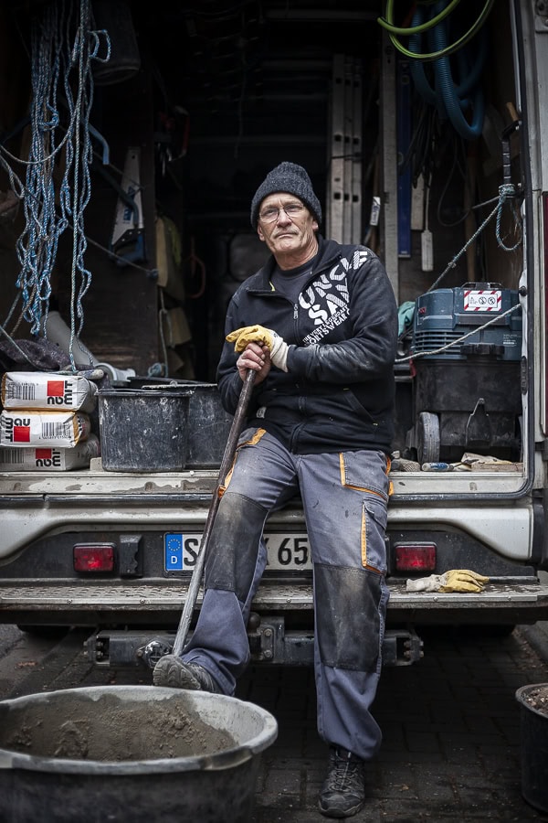 Handwerker steht mit Schaufel vor einem Werkzeugwagen, bereit für die Arbeit.