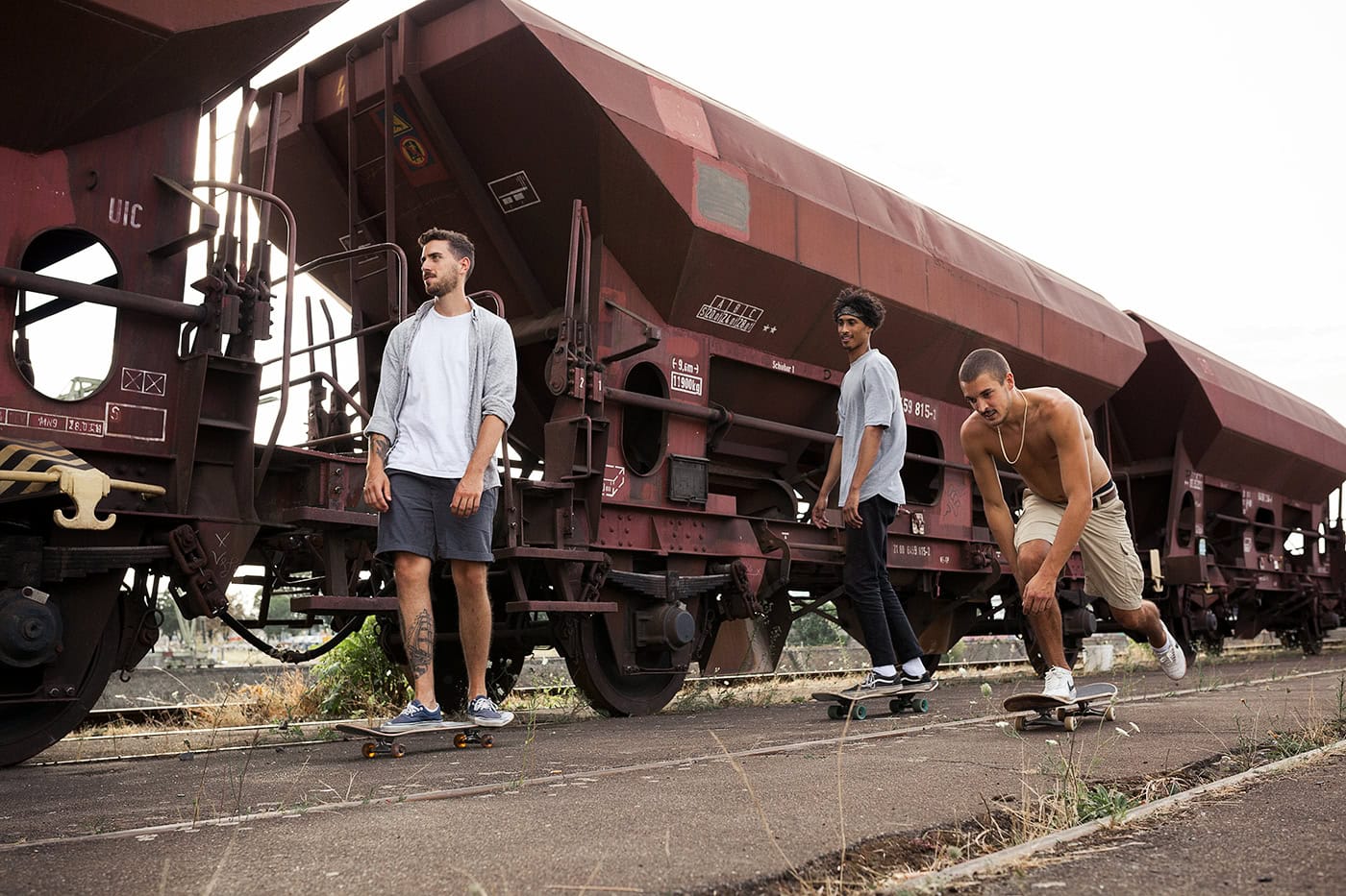 Drei junge Männer posieren neben einem alten Güterwagen in Köln, kreative Fotografie.