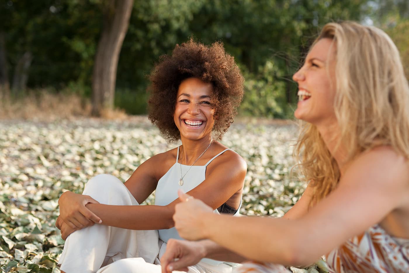 Zwei Frauen lachen und genießen die Natur im Park, entspannte Atmosphäre.