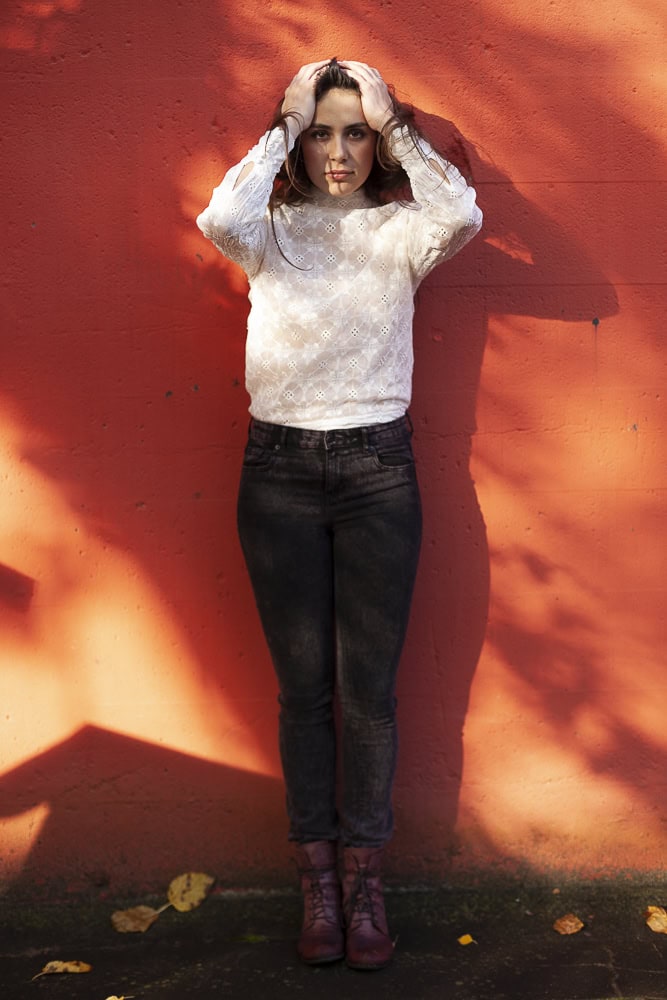 Frau in weißem Pullover und schwarzen Jeans vor roter Wand, kreative Portraitaufnahme.