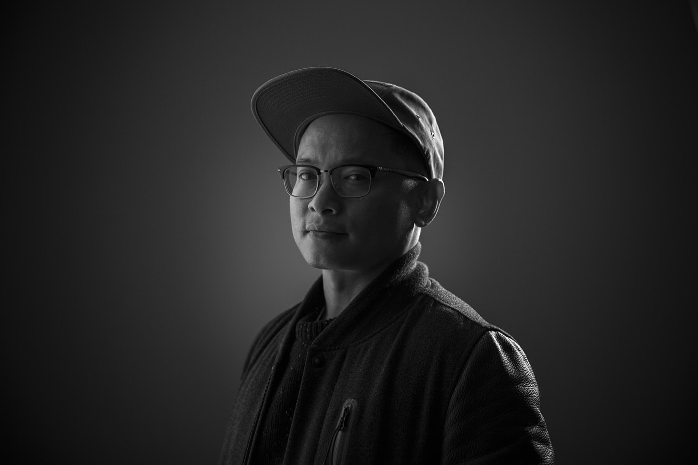 Portrait eines Mannes in Schwarz-Weiß, trägt Cap und Brille, professionelle Fotografie.