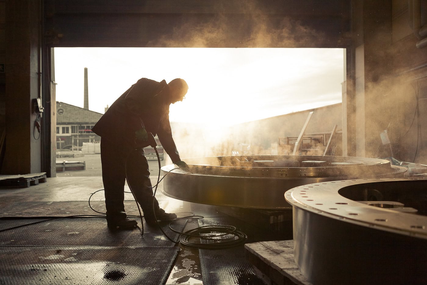 Handwerker beim Schmieden großer Metallteile in der Werkstatt bei Sonnenlicht.