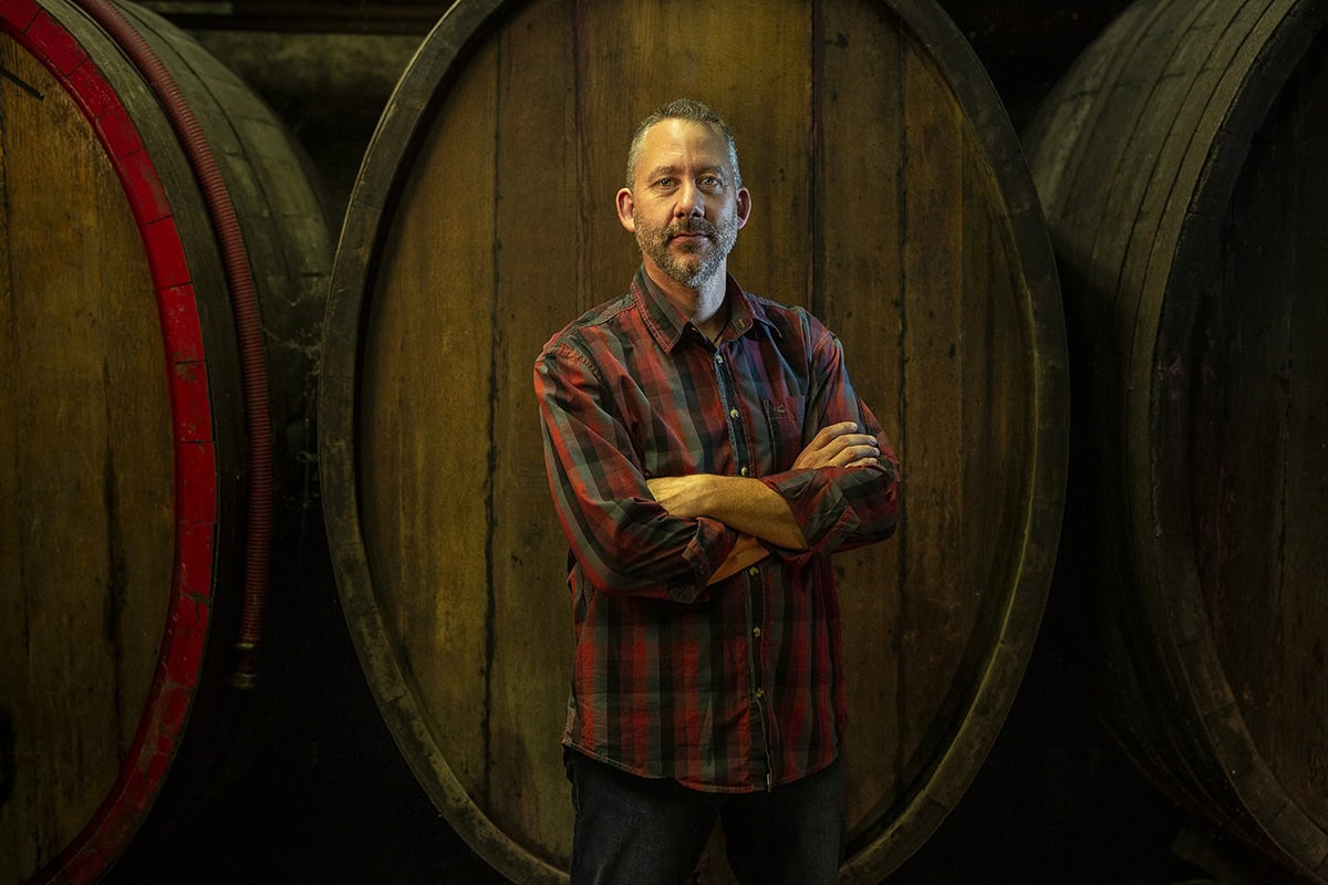 Portrait von Michael Zellmer vor Weinfässern in einer Weinkellerei in Köln.