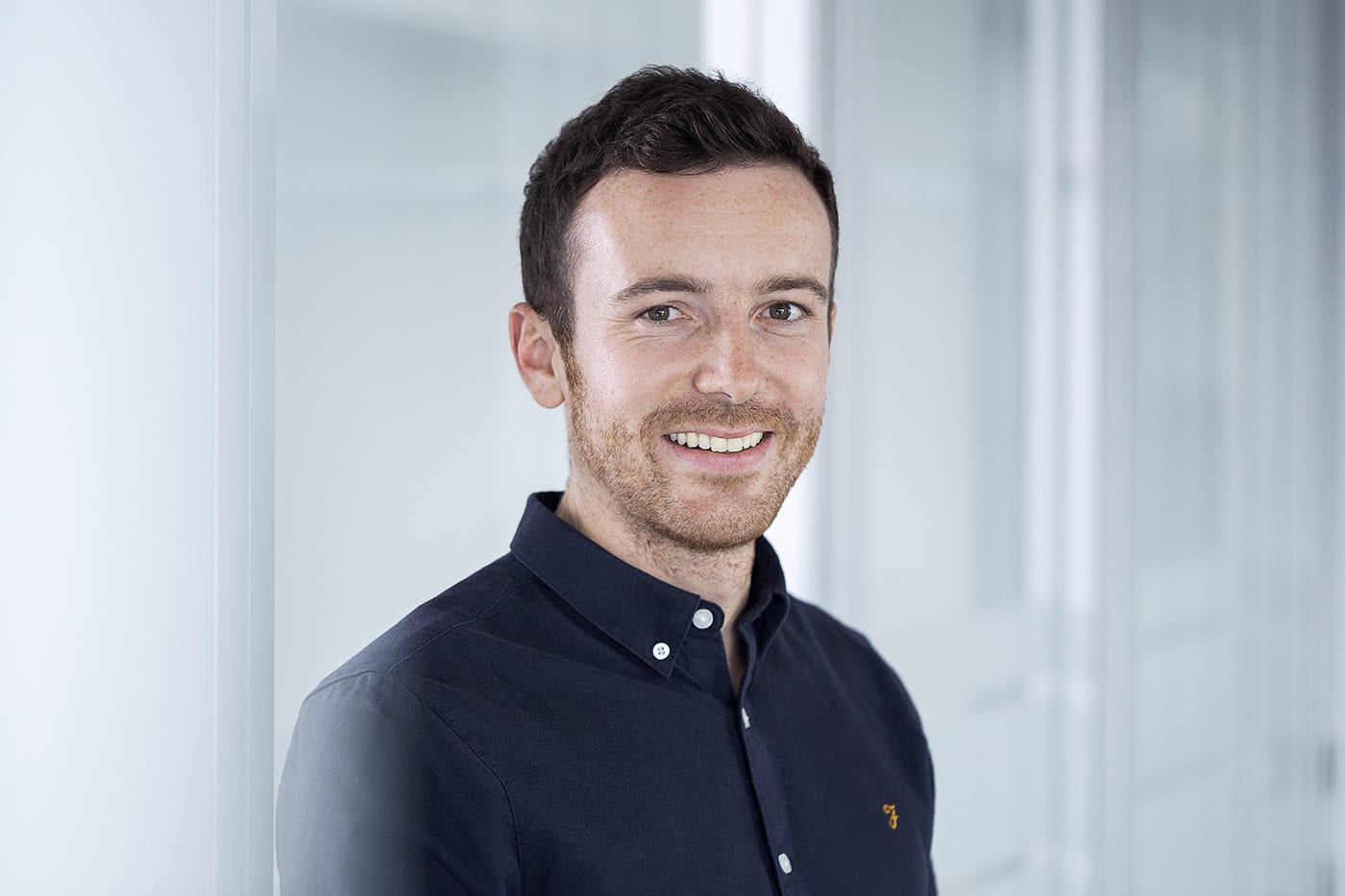 Portrait eines Mannes in Businesskleidung vor moderner Büro-Umgebung.