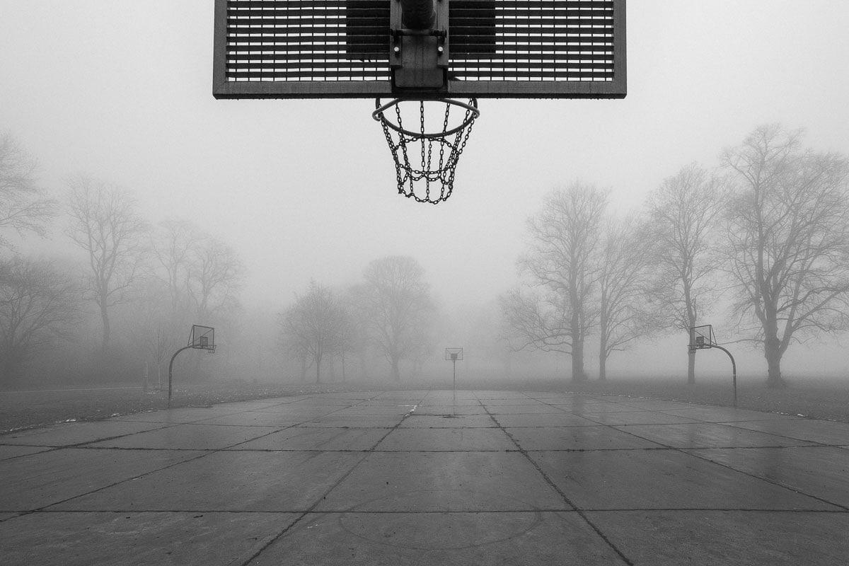 Leeres Basketballfeld im Nebel mit Korb und Banden, atmosphärische Stimmung.