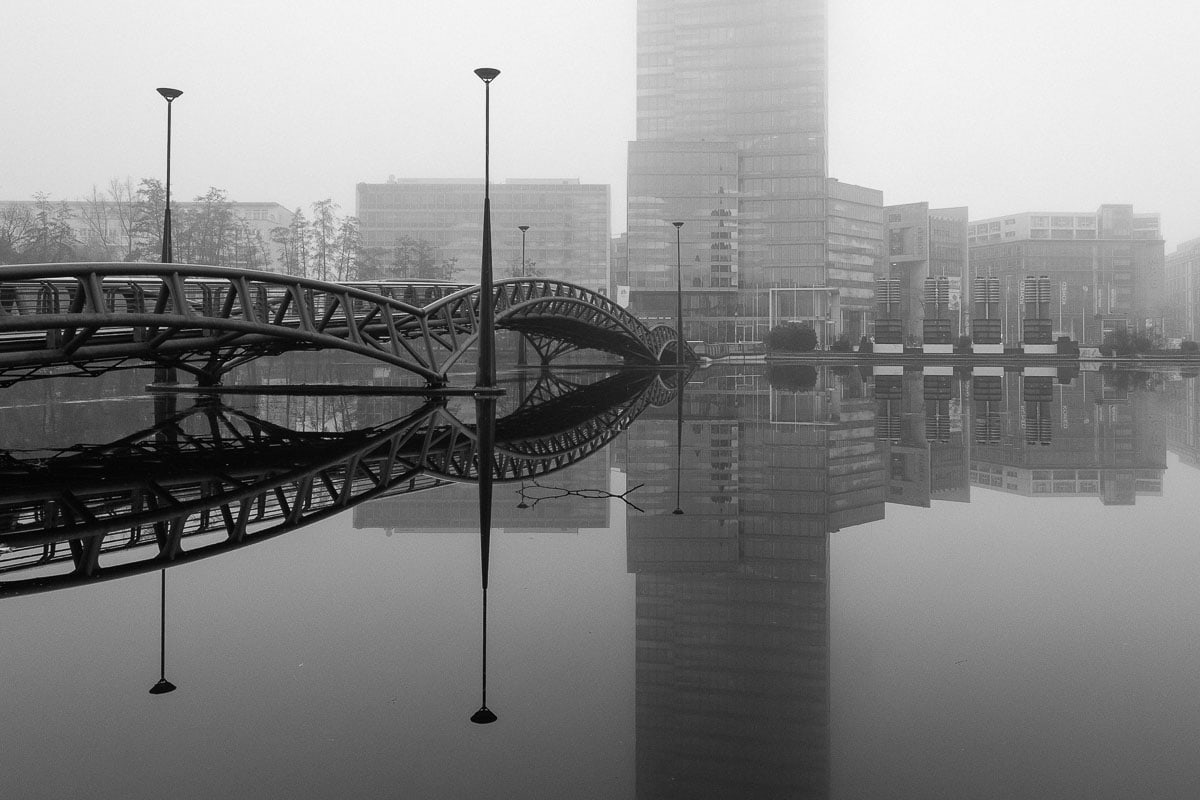 Kölner Stadtansicht mit moderner Architektur, Brücke und Wasserreflexion.
