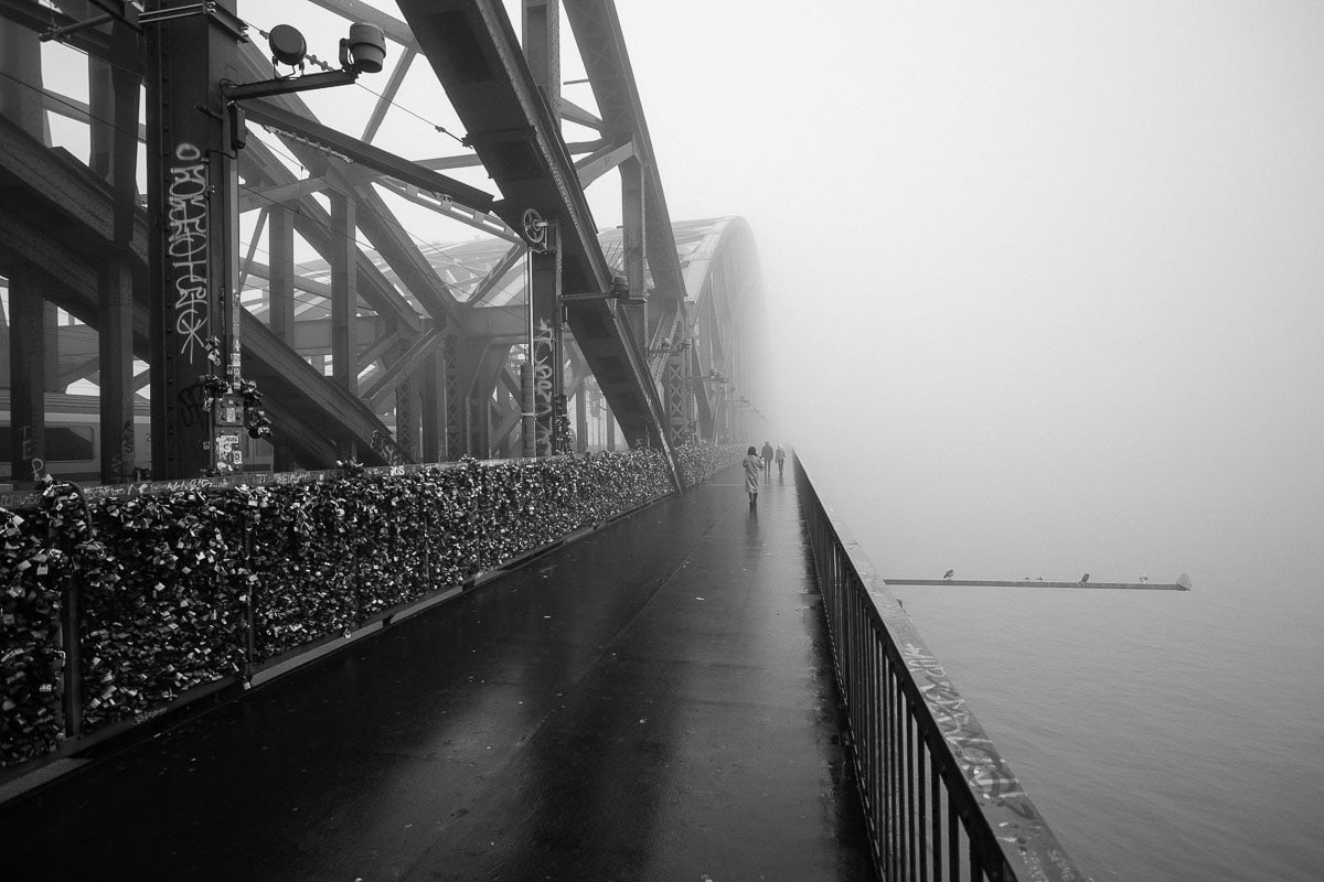 Nebelverhangene Rheinpromenade in Köln, stimmungsvolle Schwarz-Weiß-Aufnahme.