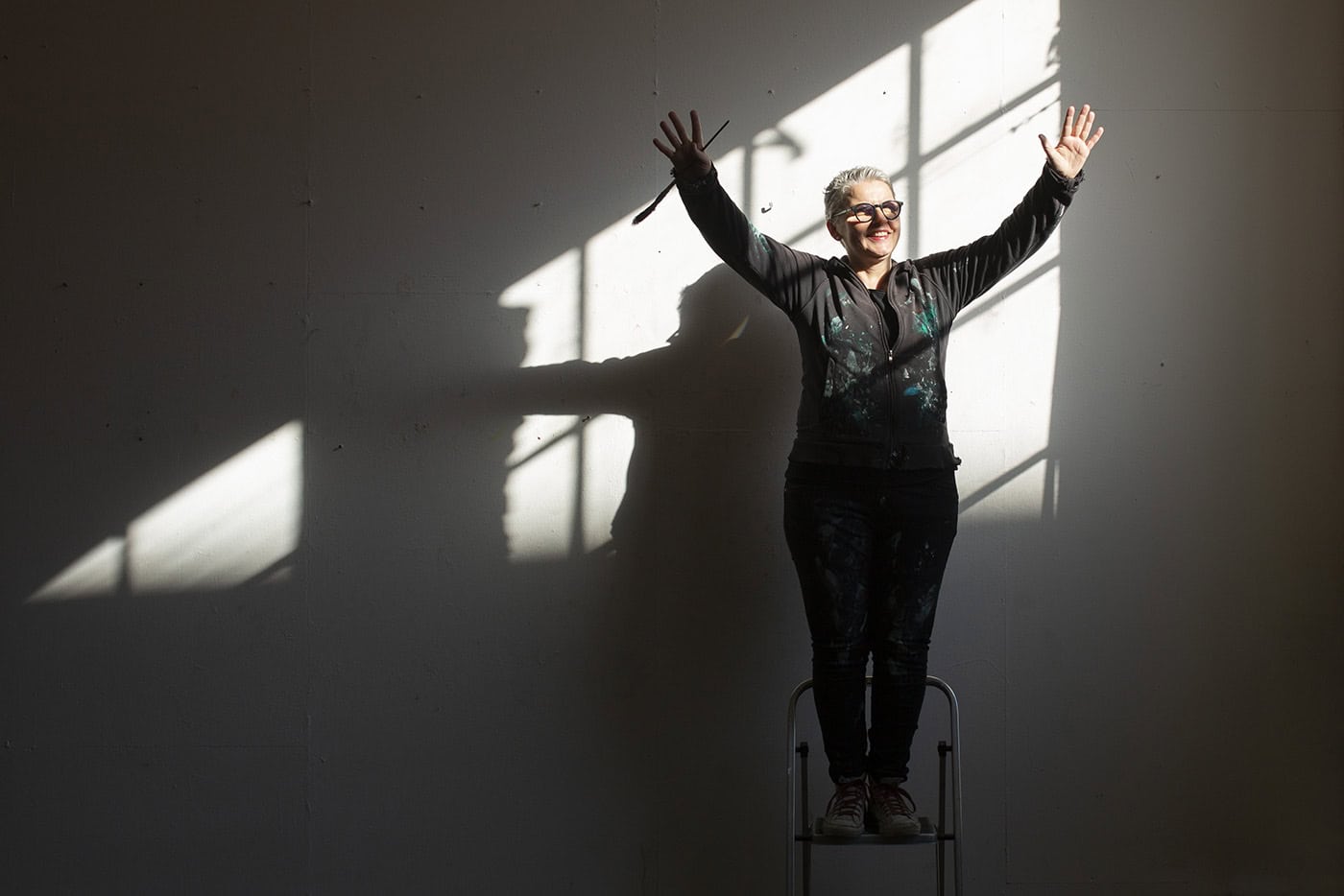 Frau steht auf einem Stuhl mit erhobenen Armen vor einer Sonnenlichtquelle, kreative Fotografie in K.