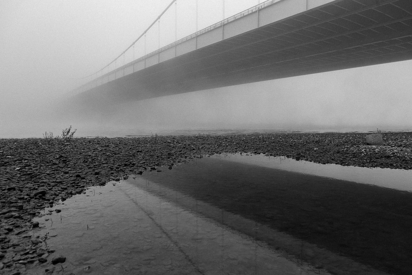 Mystische Brücke im Nebel über einem Fluss in Köln, Schwarz-Weiß-Fotografie.