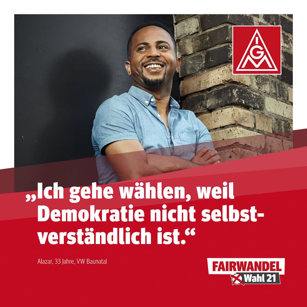 Fotografie eines lachenden Mannes vor einer Ziegelmauer, Wahlplakat im Hintergrund.
