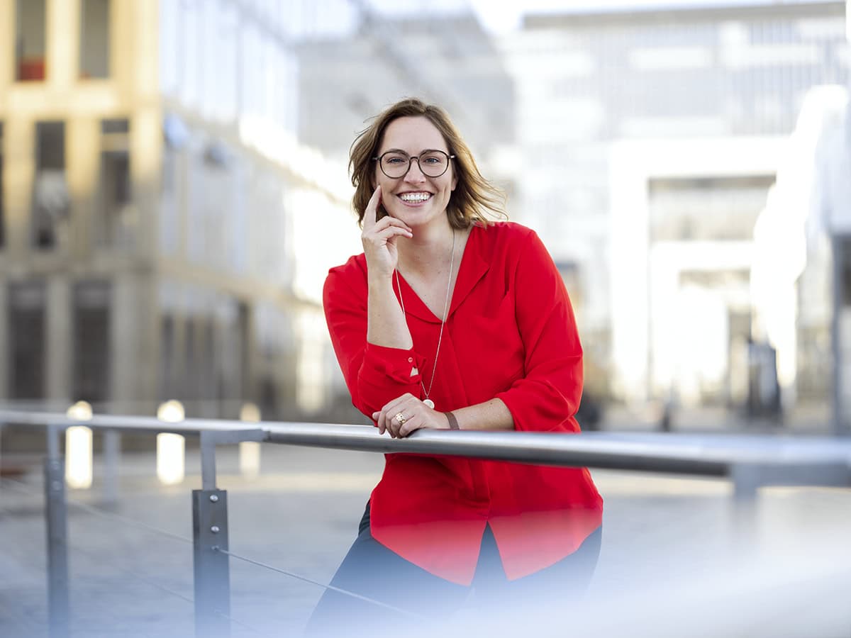 Frau in rotem Blazer lächelnd bei Stadtaufnahme, professionelle Fotografie.