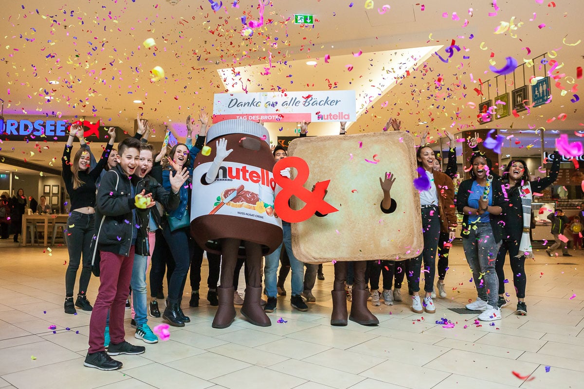 Menschen feiern mit Nutella- und Toast-Maskottchen im Einkaufszentrum.