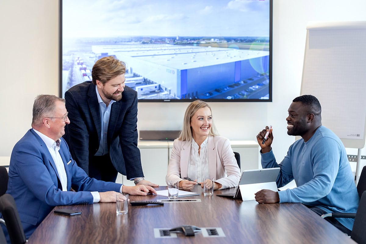 Vier Personen unterschiedlicher Altersgruppen und Herkunft bei einer Besprechung im modernen Konferenzraum mit Bildschirm und Flipchart