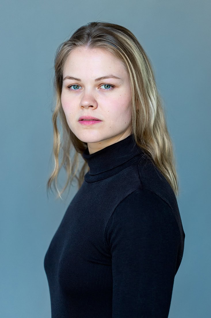 Porträt einer jungen Frau mit blonden Haaren und blauen Augen, professionell fotografiert.