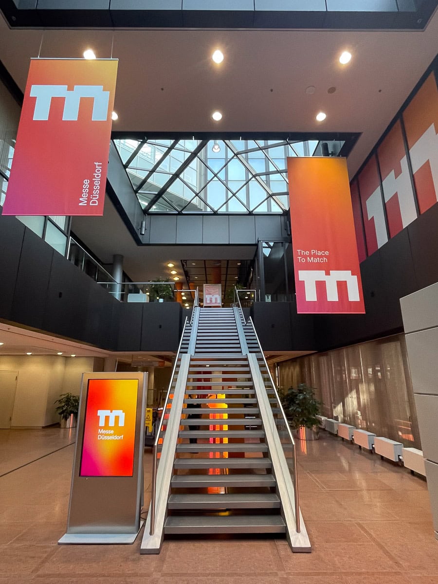Innenaufnahme einer Messehalle mit Banner, Treppe und moderner Architektur.