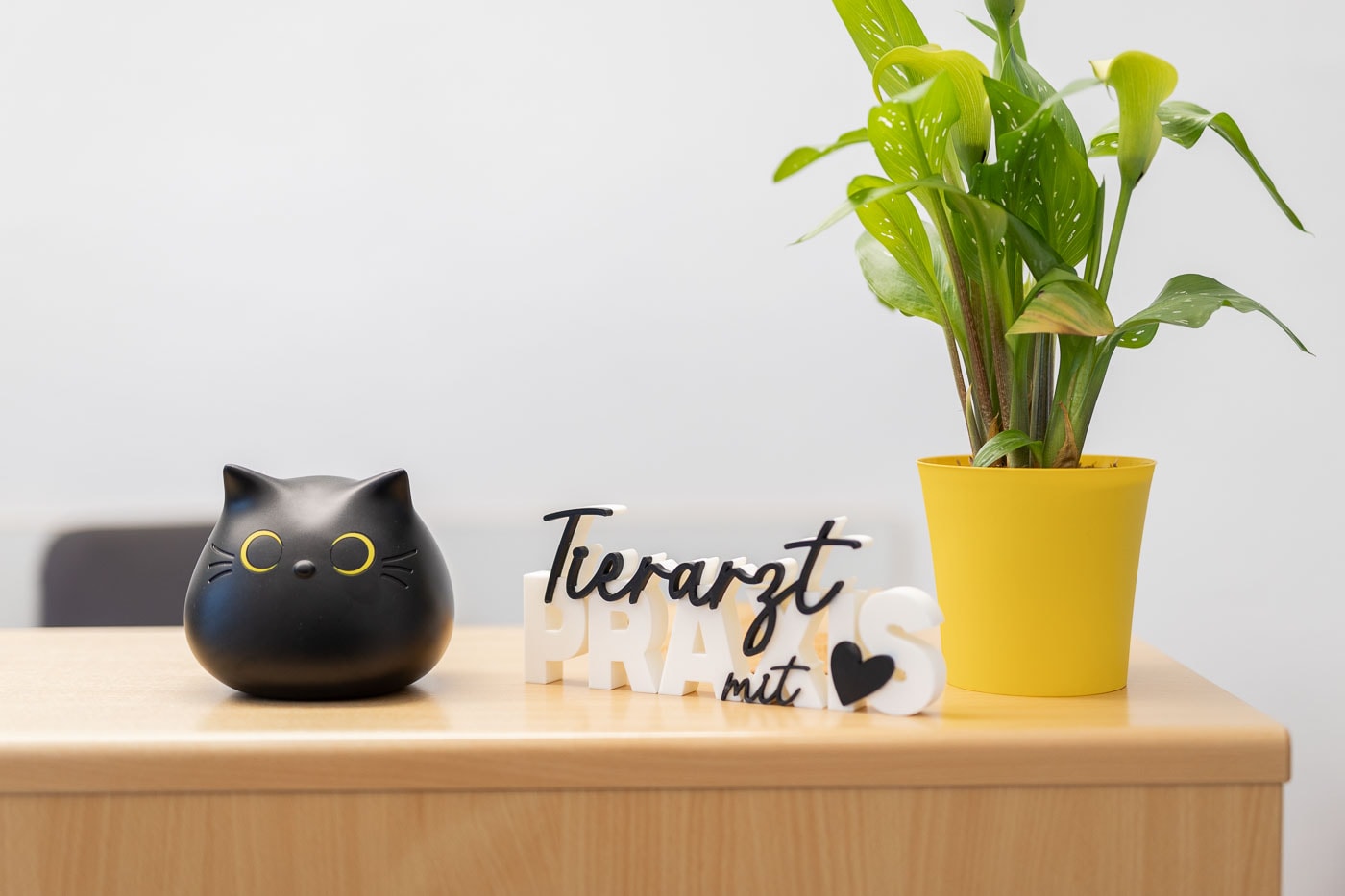 Blumen in einer gelben Vase, Katzenfigur und dekorative Schriftzüge auf einem Tisch.